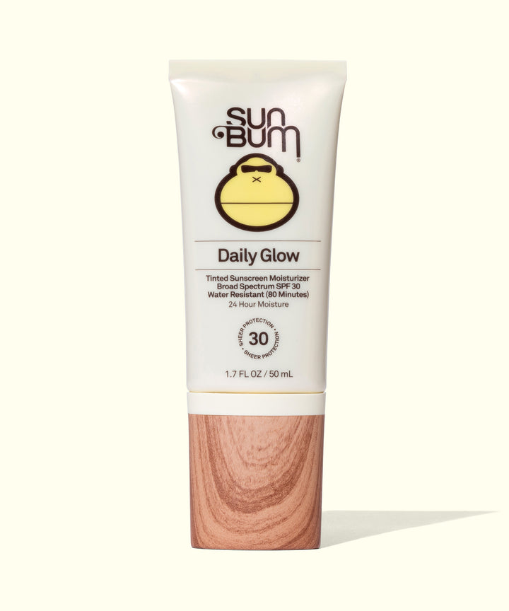 White tube of Sun Bum Daily Glow moisturizer with SPF 30, featuring a cute monkey logo and wooden-textured base, promising 24-hour hydration and dewy finish. Sun Bum