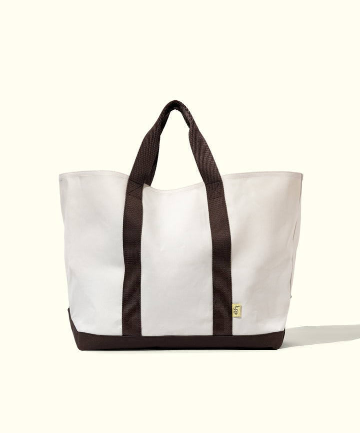 White beach tote bag with brown handles and bottom, designed for versatile carrying needs. Sun Bum.