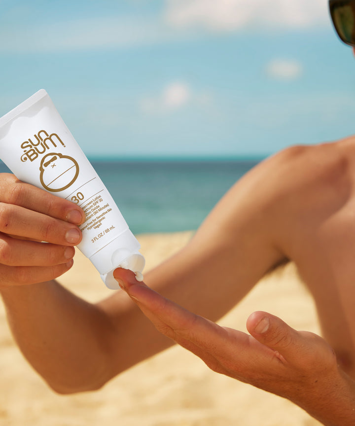 Man applying zinc-based, Fragrance Free Mineral SPF 30 Sunscreen Lotion on the beach for Broad Spectrum protection, Sun Bum.