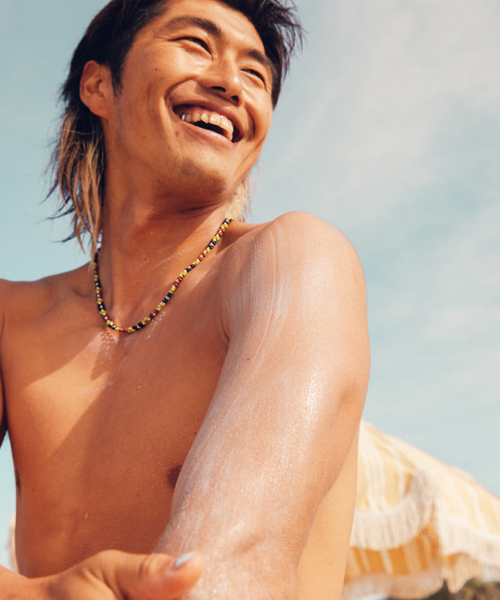 Man happily applying Original SPF 30 Sunscreen Lotion at the beach, Sun Bum