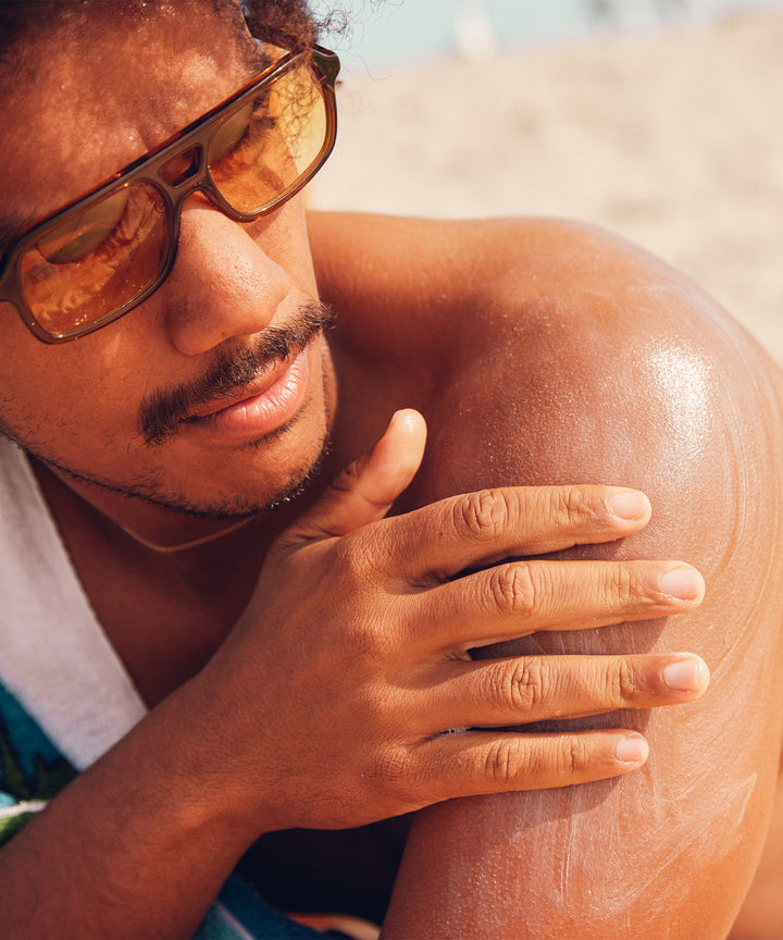 Person applying Original SPF 50 Sunscreen Lotion at the beach, keeping protected with Sun Bum.