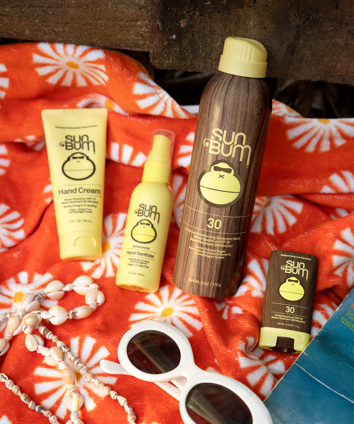 Sun Bum Original SPF 30 Sunscreen Face Stick shown with other Sun Bum skincare products on a beach towel.