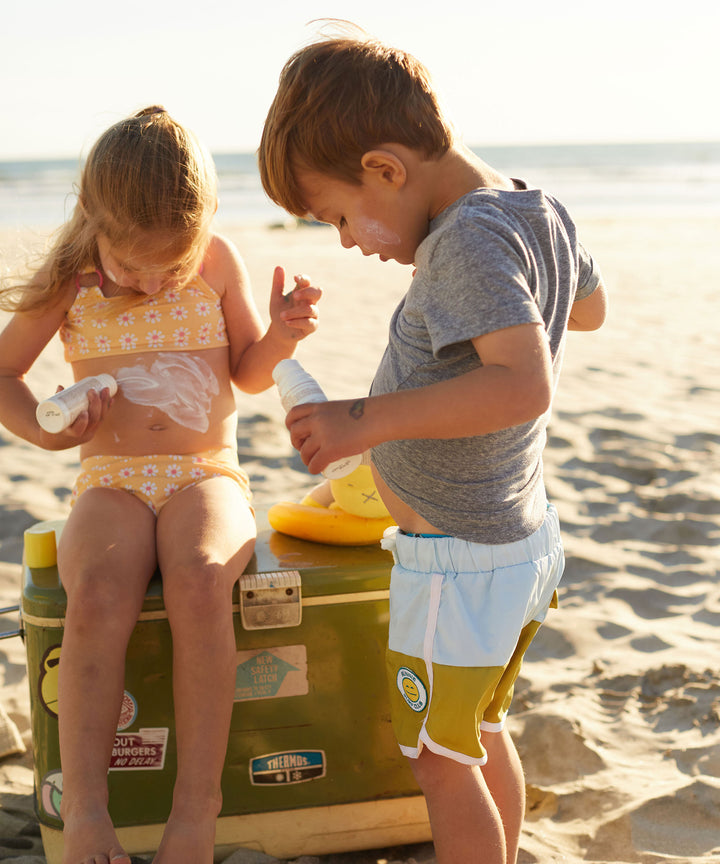 Children applying Baby Bum Mineral SPF 50 Roll-On Sunscreen on a sunny beach day, Baby Bum.